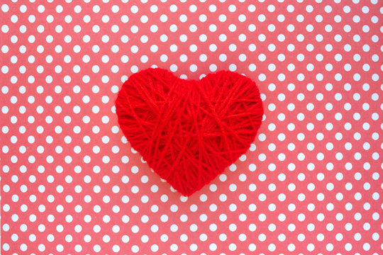 Heart of red threads on a background of cloth in polka dots. Red heart shape made from wool on textile red and white polka dots background. Yarn heart shape symbol. Concept of love, Valentines day