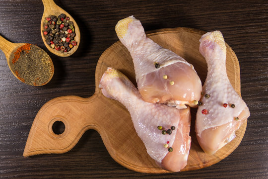 Raw chicken legs with spices on wooden cutting board on a table