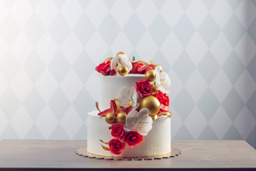 Beautiful two-tiered white wedding cake decorated with red roses. Concept of elegant holiday desserts