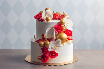 Beautiful two-tiered white wedding cake decorated with red roses. Concept of elegant holiday desserts