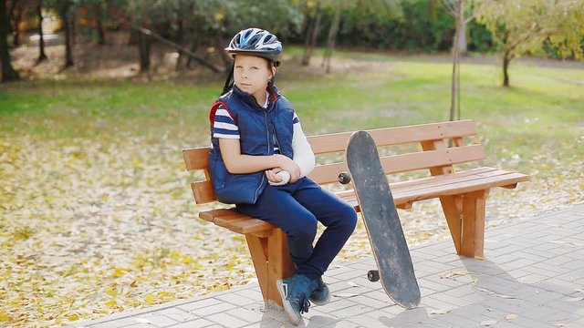 Caucasian child with broken arm sitting on the bench with skate. Failure concept.