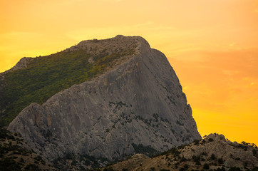 high gray mountain with a flat slope covered with greenery in orange yellow light dawn of the sun