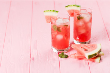 Watermelon lemonade with ice and mint leaves. Homemade lemonade of ripe berry with red and green ripes. Glass of cold watermelon tea. Refreshing summer drink. Cocktail on a wooden background