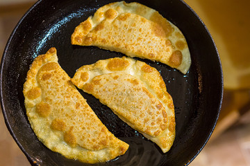 delicious fried pies with meat and greens cheburek in a pan with oil close-up