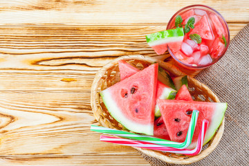 Watermelon lemonade with ice and mint leaves. Homemade lemonade of ripe berry with red and green ripes. Glass of cold watermelon tea. Refreshing summer drink. Cocktail on a wooden background