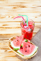 Watermelon lemonade with ice and mint leaves. Homemade lemonade of ripe berry with red and green ripes. Glass of cold watermelon tea. Refreshing summer drink. Cocktail on a wooden background