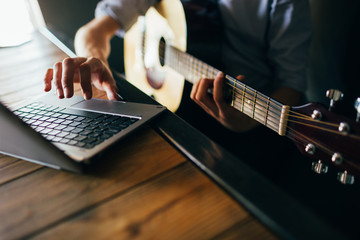 online music courses. young man learns how to play guitar through the internet. modern technology...