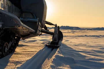 Fotobehang A snowmobile stands on the snow at sunset. © river34
