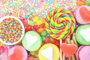 Fototapeta na wymiar Mix of confectionery and sweeties: sugar confetti, bonbon, lollypop, jelly, candy, macaron, sugar heart cube, selective focus