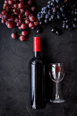 Taste red wine. Bottle of red wine, glass and black grape on black stone background top view