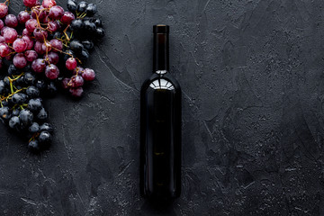 Wine bottle near bunches of red and black grapes on black background top view copyspace