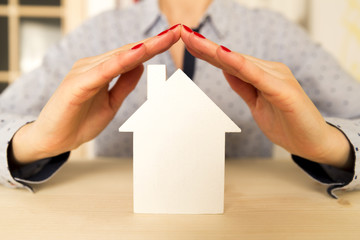 Woman holding her hands above white small model house as a sign of home protection and insurance