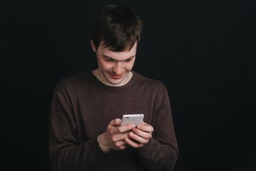 A man looks at a mobile phone screen and dials the message , the portrait of a man close up in Studio on dark background