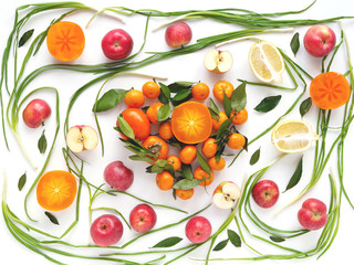 Creative flat layout of fruit, top view. Sliced  lemon, red apples, persimmon, tangerine, green onion, green leaves isolated on white background. Food wallpaper, composition pattern of fresh fruits.	