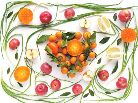 Creative flat layout of fruit, top view. Sliced  lemon, red apples, persimmon, tangerine, green onion, green leaves isolated on white background. Food wallpaper, composition pattern of fresh fruits.	