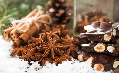 Christmas spices cinnamon, anise stars and dark chocolate with hazelnuts and background of cone and fir tree. Holiday concept of winter