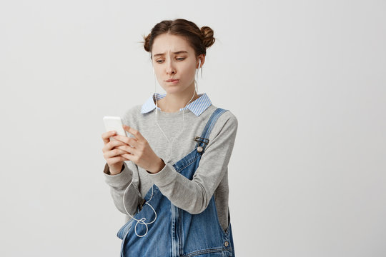 Upset Trendy Girl Looking On Smartphone With Regret Gaze And Pursed Lips. Brunette Woman Can't Find Favourite Music In Her Gadget Trying To Upload It. Technics Concept