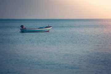 Beautiful seascape view of fishing boat floating on the sea with sunset light in the background. (Selective focus)