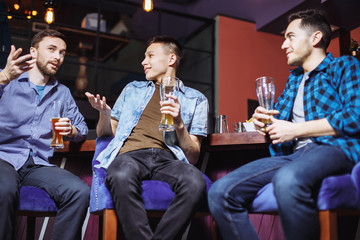 People, men, leisure, friendship and celebration concept - happy male friends talking and drinking beer at bar or pub.