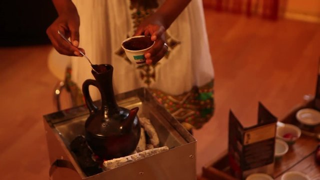 Ethiopian girl prepares coffee in traditional authentic ceramic jebena coffeepot. Coffee ceremony.