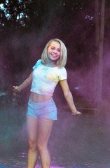 Cheerful blonde woman jumping with Holi powder exploding around her
