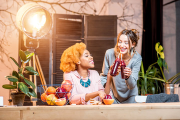 Beautiful multi-ethnic female friends sitting with healthy food and drinks indoors at the modern cozy home interior
