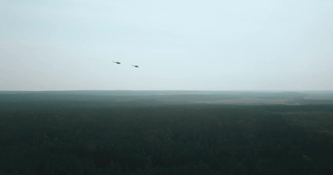 Aerial view of two helicopters flying close. Military aircraft flying in formation over green forest to city far away.