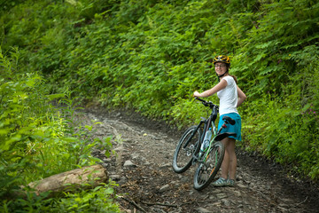 Naklejka premium Biker pushes bicycle up in the green forest