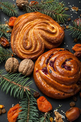 Obraz na płótnie Canvas Sweet homemade Christmas gingerbread and buns on a black background with nuts, dates, raisins and dried apricots with the branches of the Christmas tree.