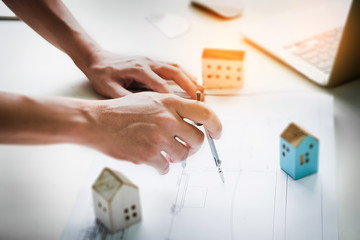Young engineers using dividers of drawing house building stucture  before presenting it at the conference with house model and computer laptop  work. Architecture design concept.