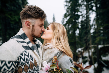 Beautiful young couple are kissing in the snowy forest