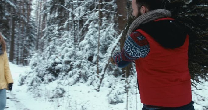 TRACKING Beautiful Caucasian couple or family bringing a Christmas tree back home from forest. Holidays, lifestyle. 4K UHD 60 FPS SLO MO