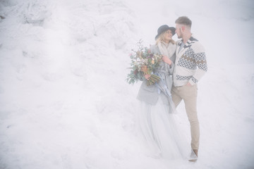 Happy young couple stand in the snowy foggy landscape, wedding bouquet in girl's hands