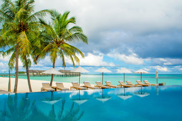 Large infinity pool on the shores of the Indian Ocean with sunbeds and umbrellas in the shade of the palm trees