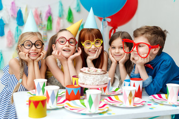 Portrait of funny group of children wear party caps, big spectacles, look with big appetite on birthday cake, want to taste it, have special occasion, spend time happily. Celebration, holidays concept