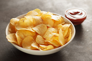 Big bowl with crispy potato chips and tomato dip sauce on table.