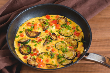 Omelette with zucchini, red paprika and chives. Frittata in frying pan on wooden board.