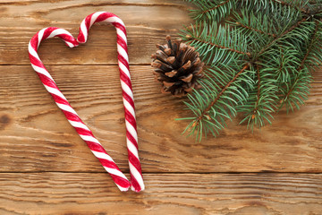 Candy sticks in heart shape on wooden table with fir-tree branch and cone as christmas background