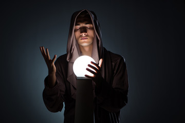 Young wizard with crystal ball in dark room