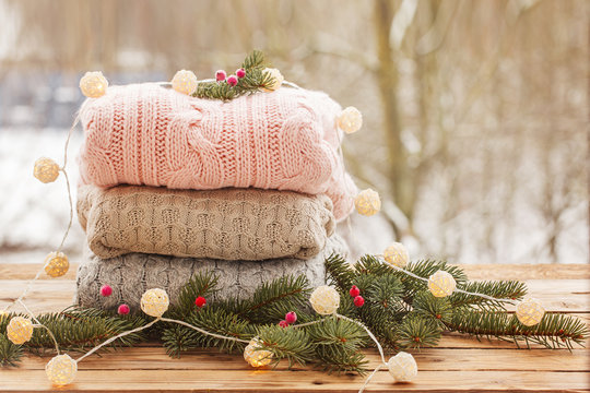 Cozy pile of knitted sweaters on wooden table on winter nature background.