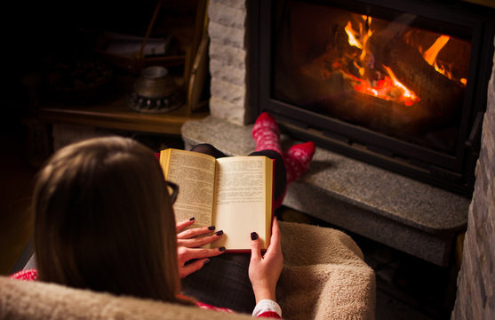 Female reading a book by the fireplace