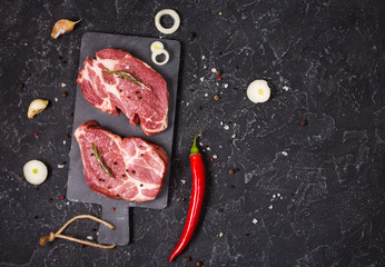 Fototapeta na wymiar Raw meat steak with seasonings on black stone background. Space for text. Steak ready for cooking. Barbecue concept. Ingredients for meat roasting.