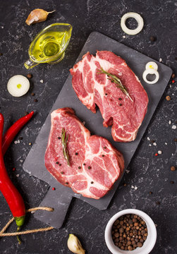 Raw meat steak with seasonings on black stone background. Steak ready for cooking. Barbecue concept. Ingredients for meat roasting.