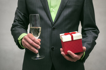 Man in suit holds in one hand a present box and champagne in wineglass in another hand isolated on white. Award ceremony.