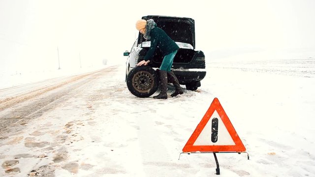 car broke, need to put the spare tire, woman talking on a cell phone, calls for help, an emergency on the road in winter, dangerous winter road covered with snow