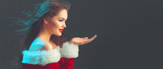 Christmas scene. Beauty model girl, wearing red santa dress, pointing hand