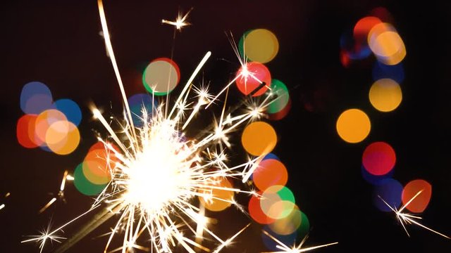 Christmas sparkler burning on a background of christmas tree with colorful bokeh and christmas lights