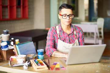 Portrait of modern tattooed woman using laptop while working in art studio, copy space