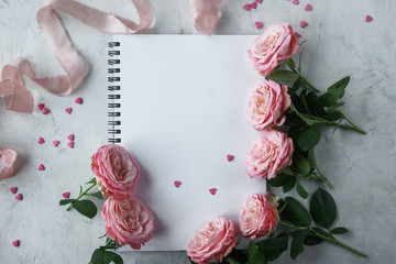 Notebook, roses, pink ribbon and sweet candies in shape of heart on white background