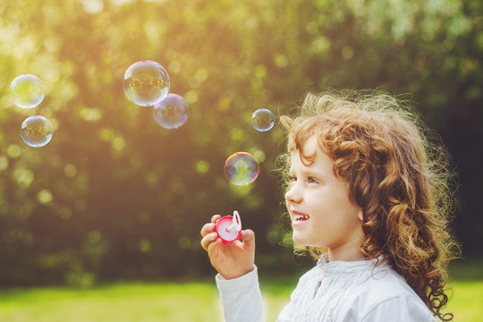 little girl blowing soap bubbles in summer park.